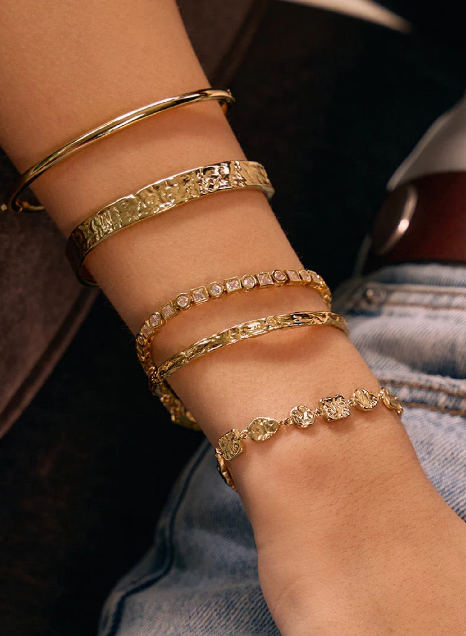Close-up of a wrist wearing multiple gold bracelets with a blurred background