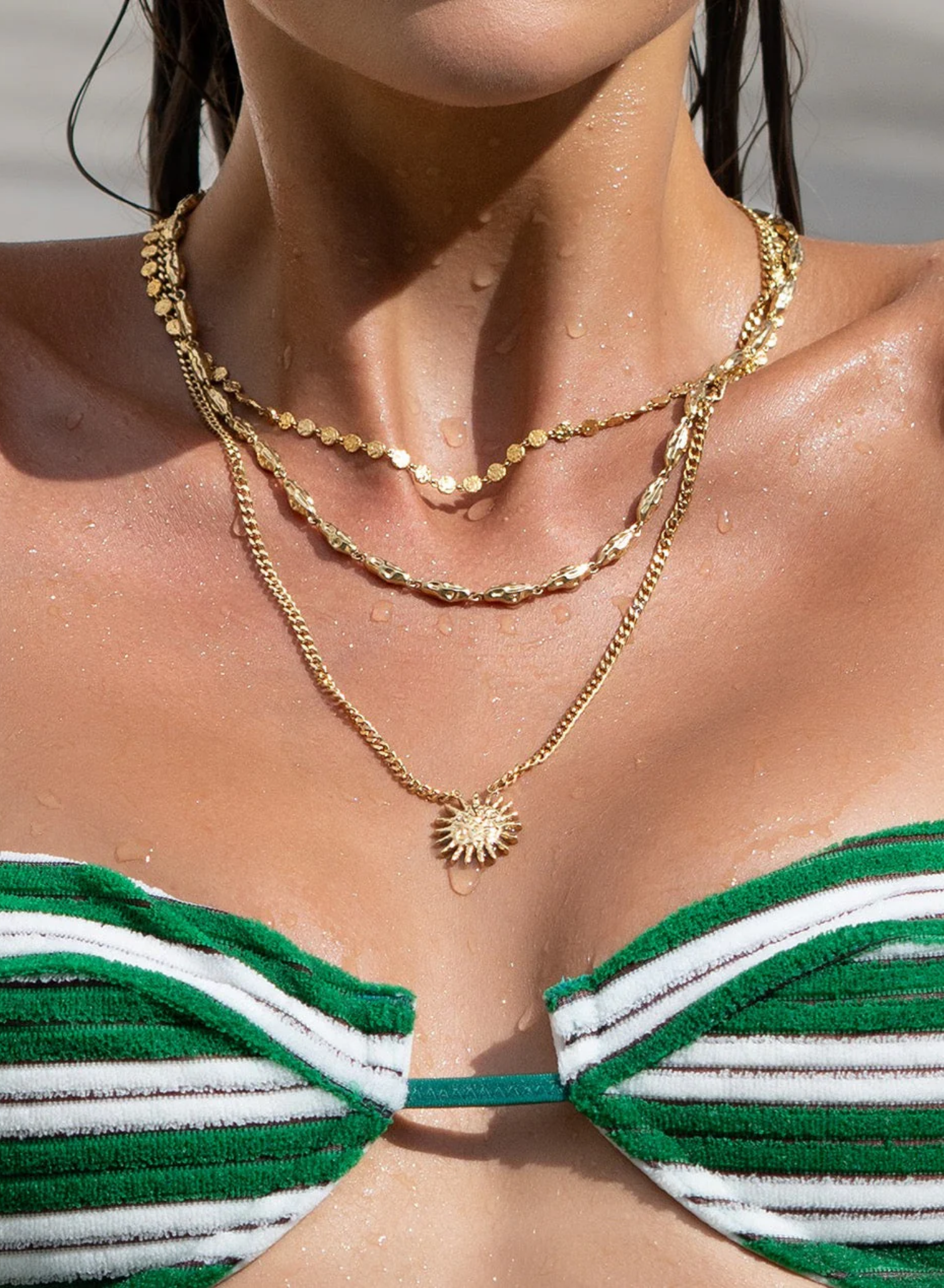 Close-up of a person wearing a green and white striped bikini top with gold necklaces.